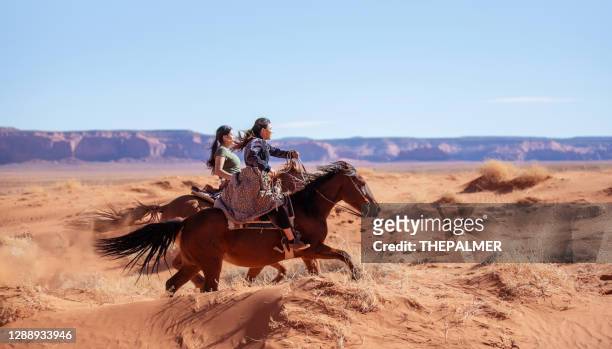 two native american indian sisters riding horses on the sand dunes of monument valley arizona - usa - horseback riding arizona stock pictures, royalty-free photos & images
