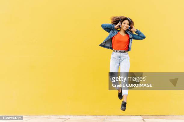 cheerful ethnic woman listening to music and jumping - young woman bright colour stock pictures, royalty-free photos & images