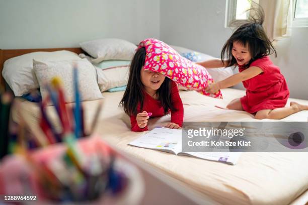 Young sister of an Asian sibling pair disturbs her sister with a one way pillow fight