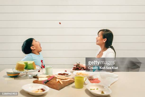 asian mother and son playing hole in one with a grape during tea time - catching food stock pictures, royalty-free photos & images