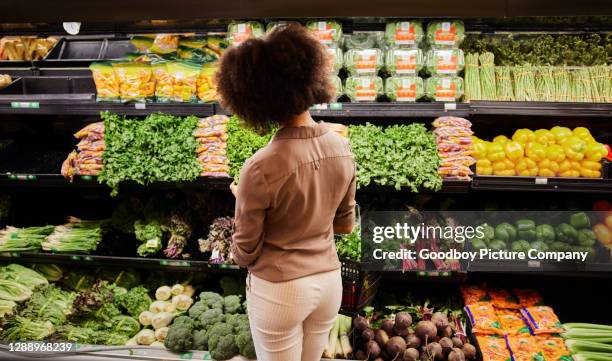 young woman looking at the produce section in a supermarket - secção de frutas e legumes imagens e fotografias de stock