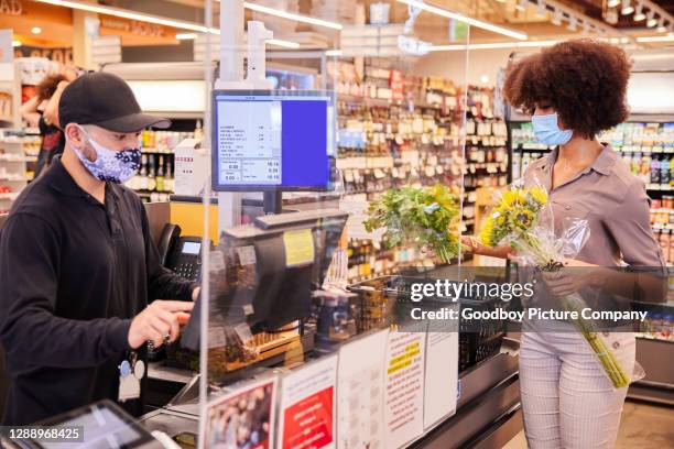 donna con una maschera protettiva per il viso in piedi in un supermercato protetto in plexiglass - cloth face mask foto e immagini stock