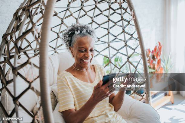 eine seniorin mit ihrer kreditkarte hält ihr handy im wohnzimmer des hauses - african woman shopping stock-fotos und bilder