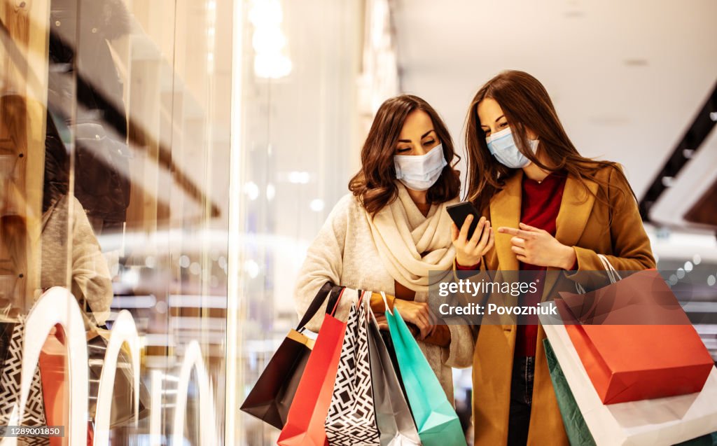 Two young girl friends in safety medical masks during shopping in the mall