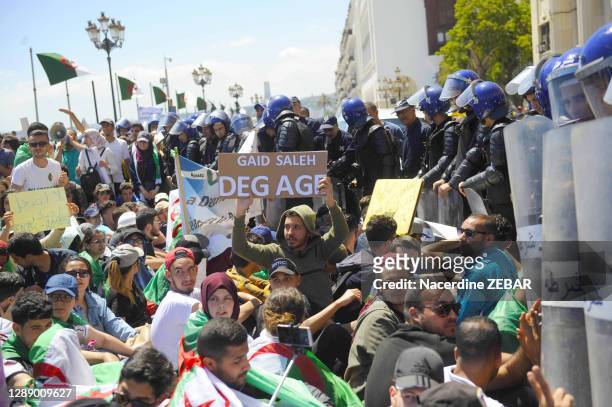 Etudiants drapés du drapeau algérien effectuant un sit-in face à un cordon de policiers et panneau "Gaid Salah" lors d'une manifestation "un vrai...
