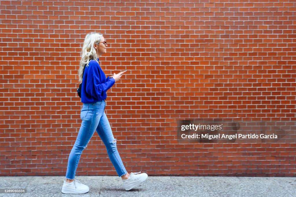Blonde girl walking with a mobile down the street