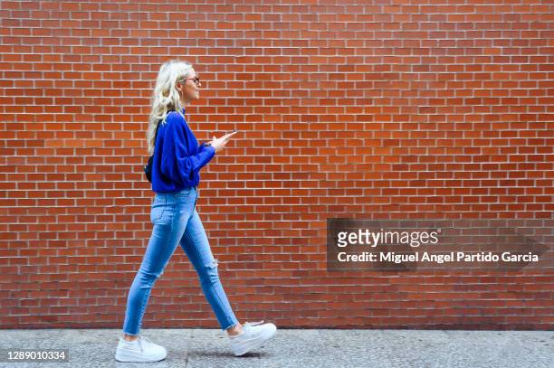blonde girl walking with a mobile down the street - slim stock pictures, royalty-free photos & images