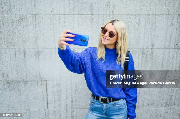 pretty blonde woman with sunglasses taking a selfie with mobile in the city - blond woman city lifestyle stock-fotos und bilder