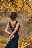 Fantasy woman lady in a black lace dress. bare open sexy back against background of an autumn forest. Elegant vintage medieval hairstyle for long hair. Fashion princess model posing. healthy dark hair