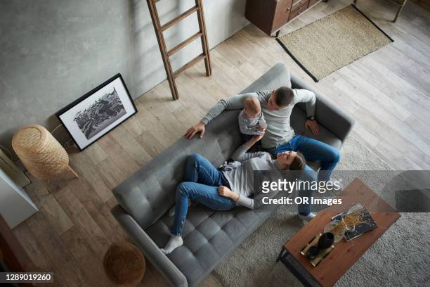 father, mother and baby girl relaxing on couch at home - overhead view photos et images de collection