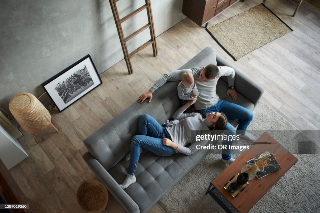 Father, mother and baby girl relaxing on couch at home