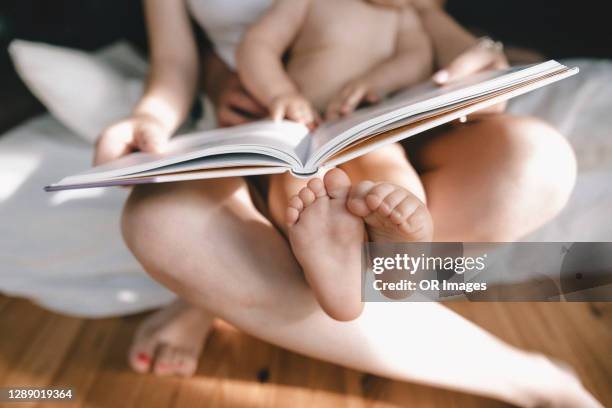feet of baby girl sitting on mother's lap with a book - baby close up bed stock pictures, royalty-free photos & images