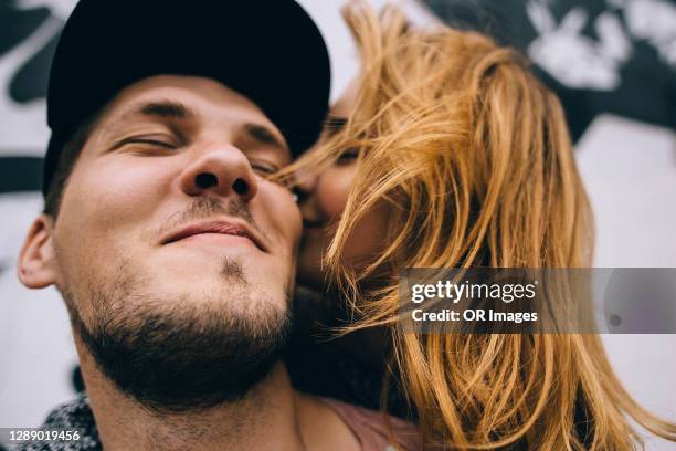 affectionate young woman kissing boyfriend with closed eyes - ungestellt stock-fotos und bilder