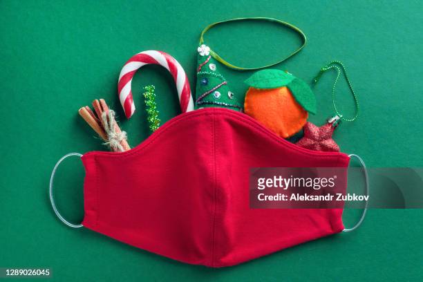 protective red medical face mask, striped sweet candy cane, handmade christmas tree toys, cinnamon, tinsel on green background. prevention and prevention of the spread of the covid 19 pandemic. the concept of a happy healthy christmas. - coronavirus winter bildbanksfoton och bilder