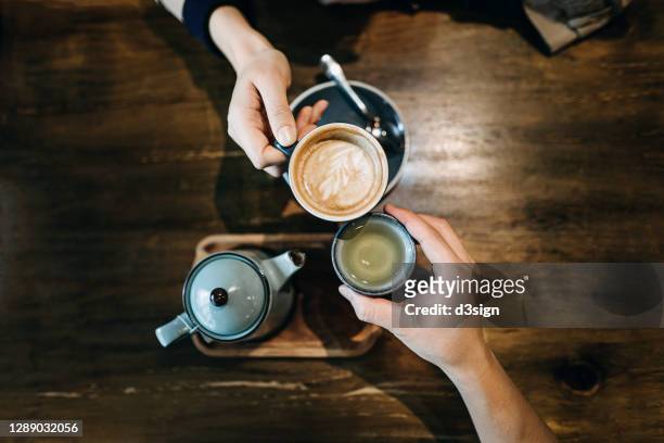 top view of young couple having a good time, toasting with a cup of coffee and tea over a rustic wooden dining table in a cafe, enjoying a celebration event - asian drinking tea stock pictures, royalty-free photos & images