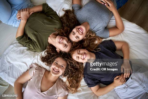 top view of four happy young women lying on bed - sister foto e immagini stock