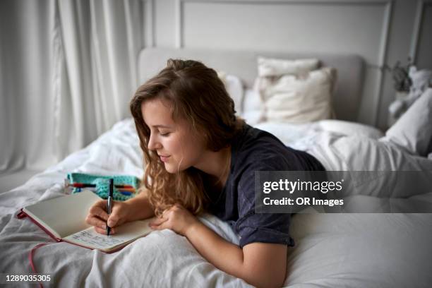 young woman lying on bed writing in diary - 2020 diary stock pictures, royalty-free photos & images