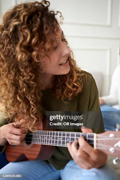 young woman playing ukulele at home - ukulele stock-fotos und bilder