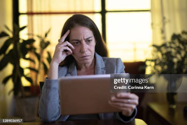 woman looking concerned while reading news on tablet - surprised woman looking at tablet stock pictures, royalty-free photos & images