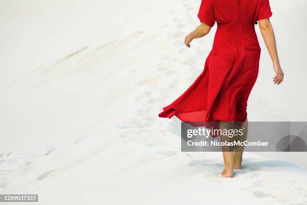 rückansicht der weiblichen, die barfuß in weißer sanddüne spazieren geht - red dress stock-fotos und bilder