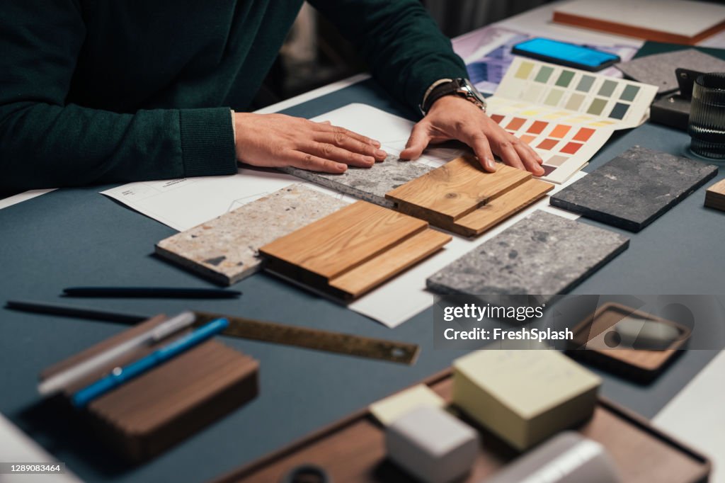 Mani di un interior designer anonimo maschile che confronta campioni di materiali diversi nel suo ufficio