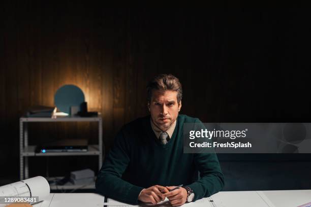 portrait of a handsome young architect sitting at the desk of his office, in front of his new project (dark background, copy space) - the project portraits stock pictures, royalty-free photos & images