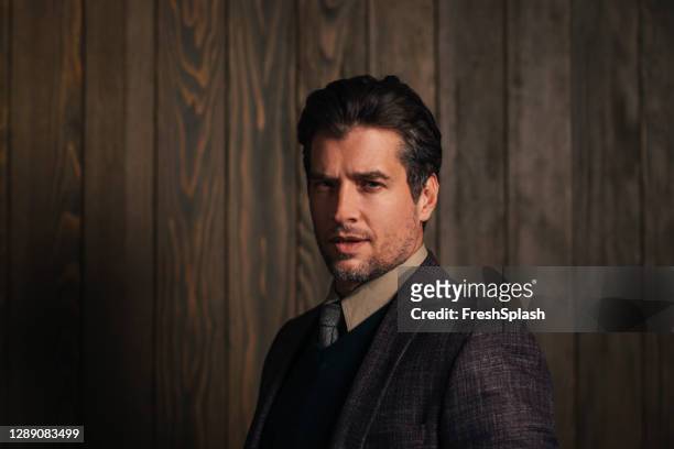 portrait of a handsome young businessman wearing a suit and a tie standing in front of a brown wooden wall - fato castanho imagens e fotografias de stock