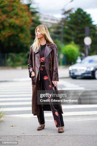 Guest wears a brown leather long coat, a black and purple tie-and-dye top, pants, brown leather pointy shoes, outside Hermes, during Paris Fashion...