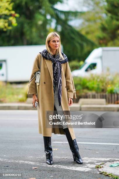 Camille Charriere wears a long scarf, a beige long wool coat, a bag, white pants, black leather high boots, outside Hermes, during Paris Fashion Week...