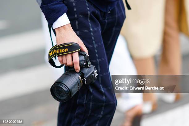 Photographer is seen wearing blue checked pants, and using a Nikon DSLR camera equipped with a Zoom lens, on October 03, 2020 in Paris, France.