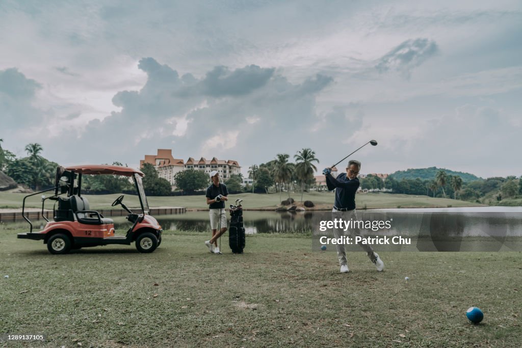 Asian chinese mature man golfer is preparing to teeing off at golf course while his son is observing
