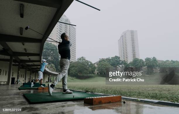 aziatische chinese rijpe mens die zijn golfclub bij drijfwaaier slingert - drivingrange stockfoto's en -beelden