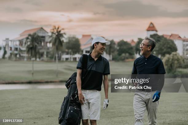 asiáticos chineses pai e filho golfistas andando e tendo boa conversa e sorrindo no campo de golfe durante o pôr do sol - golf clubhouse - fotografias e filmes do acervo