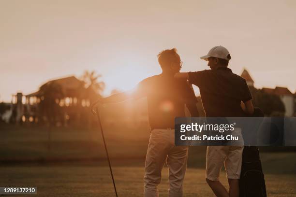 asiatische chinesische vater und sohn golfer sehen sich auf golfplatz bei sonnenuntergang - golf stock-fotos und bilder