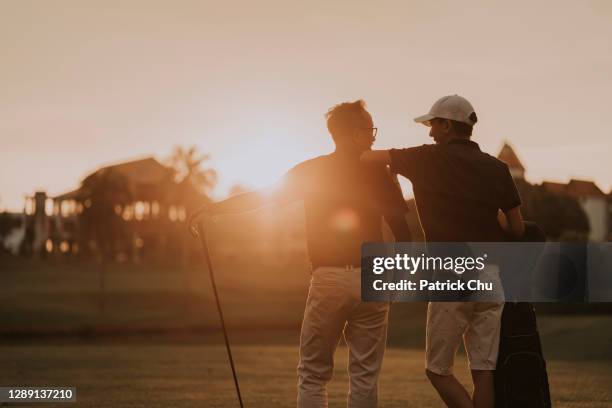 asian chinese father and son golfers looking at each other at golf course during sunset - golf shirt stock pictures, royalty-free photos & images