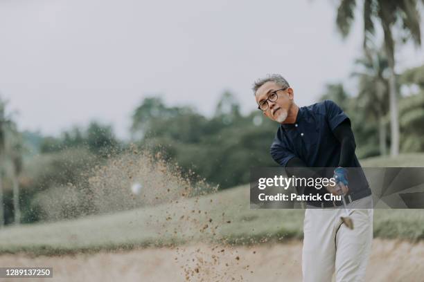 asian chinese mature man golfer hitting the ball at sand bunker - golfer stock pictures, royalty-free photos & images