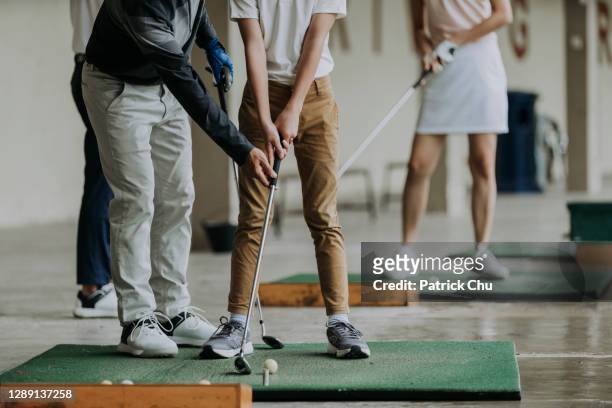 asiático chino maduro hombre sofá de golf enseñando joven estudiante masculino a jugar al golf en el campo de prácticas - golf clubhouse fotografías e imágenes de stock