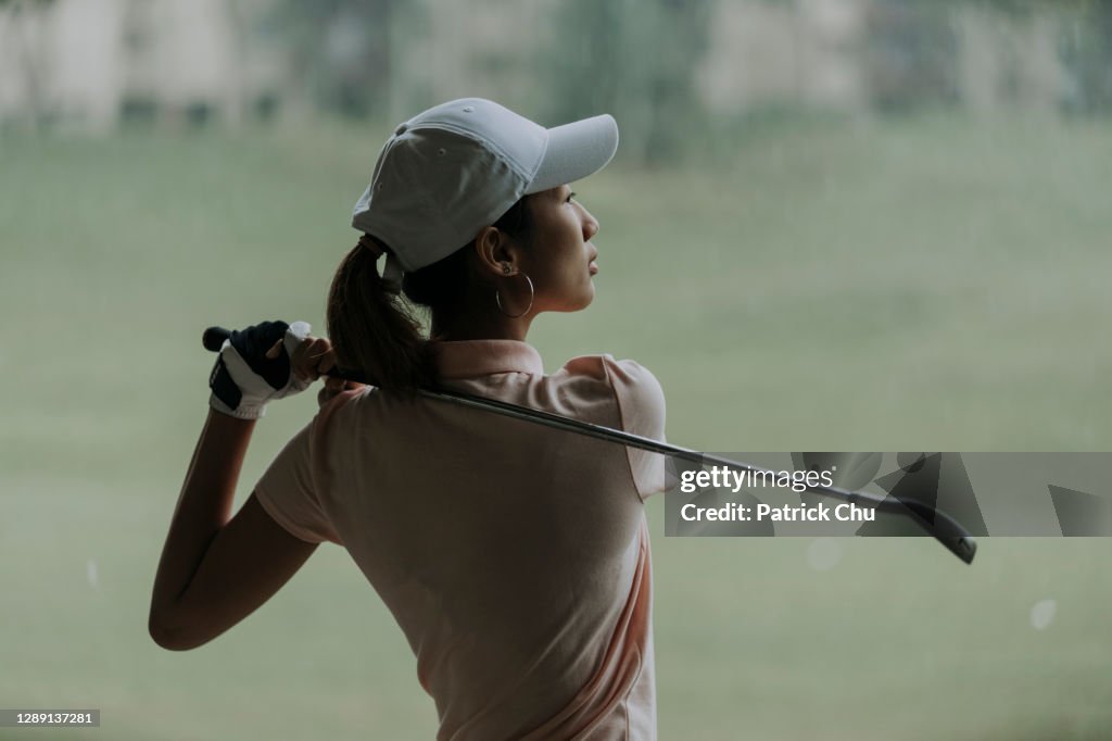 Confident asian chinese mature woman golfer swinging golf club at golf course