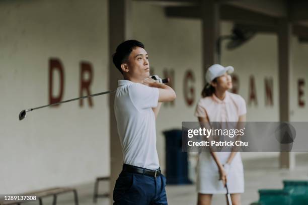 zuversichtlich asiatische chinesische reife mann golfer swinging golfclub auf driving range golfplatz - sportverein stock-fotos und bilder