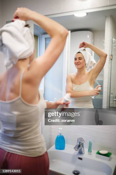 reflexion der lächelnden frau mit handtuch auf nassen haaren, sprühen deodorant unter dem erhobenen arm - deo frau badezimmer stock-fotos und bilder