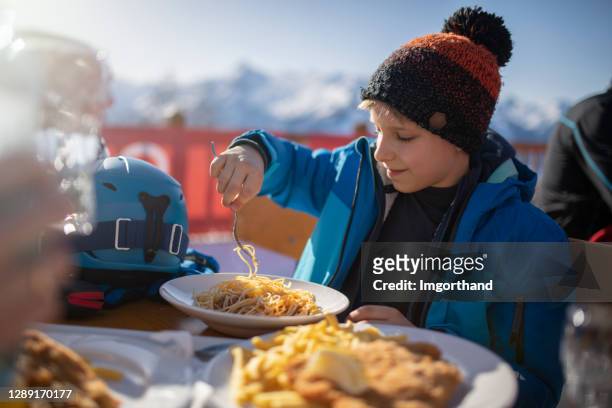 petit garçon mangeant le déjeuner dans le restaurant alpin de ski - sport d'hiver photos et images de collection