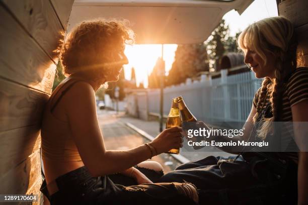 young female couple toasting with beer bottles in back of van - beer friends imagens e fotografias de stock