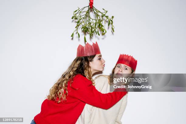 girl resisting kiss under the mistletoe from her sister - christmas angry stock pictures, royalty-free photos & images