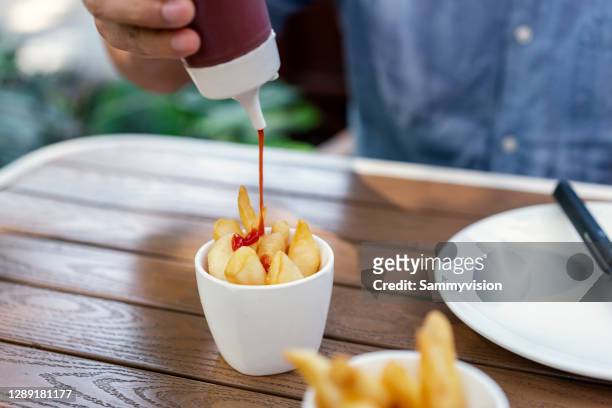 squeezing ketchup on french fries - squirt stockfoto's en -beelden