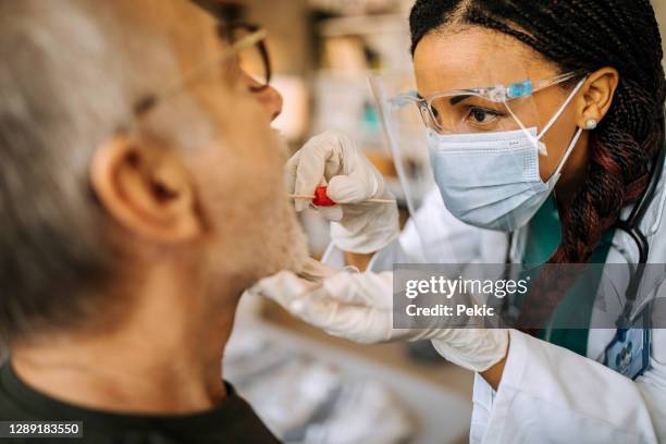 fermez-vous vers le haut de l’infirmière prenant le test d’écouvillon du patient aîné d’homme pendant la visite à la maison - coton tige photos et images de collection