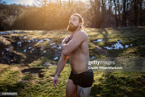 een jonge mens met lang haar en een sterk lichaam, dat zich op de kust door het meer bevindt en van een zonnige de winterdag geniet - een mens treft voorbereidingen om het ijzige water in te gaan - bathing in sunset stockfoto's en -beelden