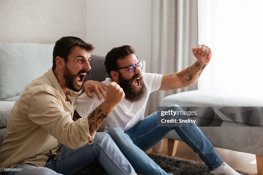 Two friends cheering, watching sport event on TV.