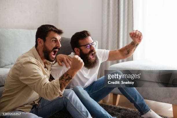 two friends cheering, watching sport event on tv. - match sport stock pictures, royalty-free photos & images