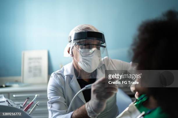 zahnarzt untersucht zähne von kind sitzen im zahnarztstuhl - gesichtsschirm stock-fotos und bilder