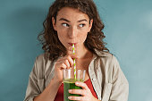 Young woman drinking detox juice with straw on blue wall